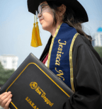 A woman holding her graduation certificate with graduation uniform